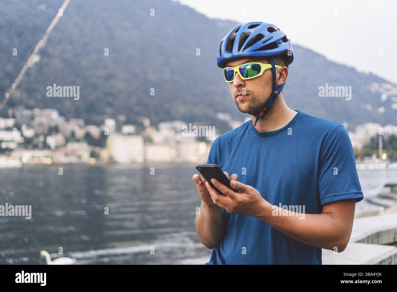Il tema del turismo e dei viaggi in Italia. Un ciclista maschile usa un telefono sulla riva del lago di Como. Turista con un casco con una bicicletta sulla riva o Foto Stock