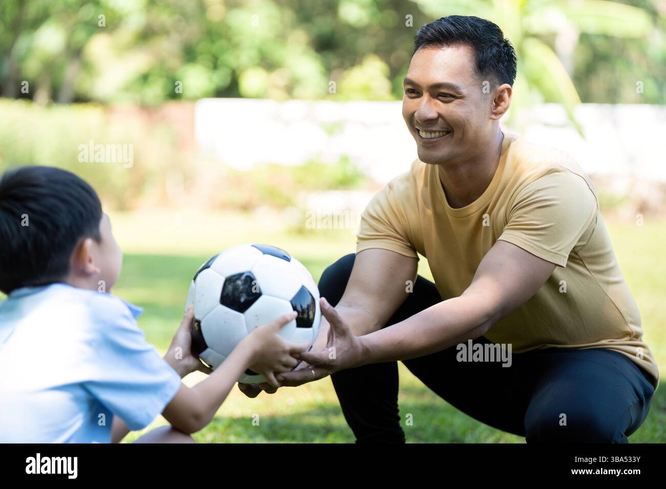 Padre e figlio trascorrono momenti di qualità insieme, dimostrando benessere e gioia mentre giocano a calcio all'aperto in un parco verde. Foto Stock