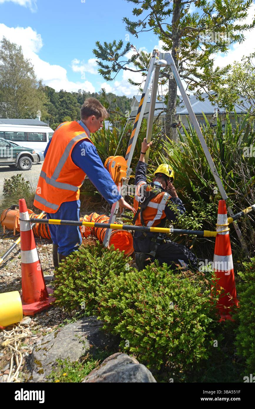 Un apprendista idraulico entra in uno spazio ristretto per un esercizio di formazione in uno scarico di acqua piovana in una proprietà commerciale Foto Stock