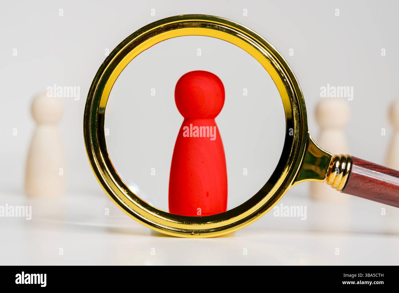 Una lente d'ingrandimento che esamina figure rosse in legno, selezionare una persona nel team, risorse umane. Reclutamento strategico. Blocchi di legno con connessione di rete Foto Stock