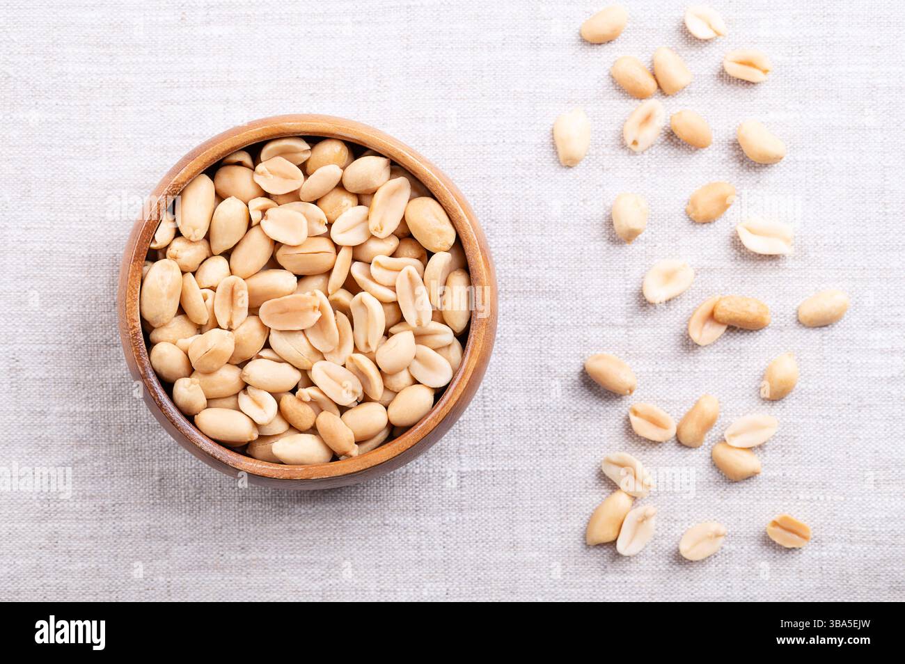 Arachidi tostate in un recipiente di legno su tessuto di lino. Snack croccanti pronti da mangiare a base di frutta di Arachis ipogaea. Noci da snack dorati leggeri. Foto Stock