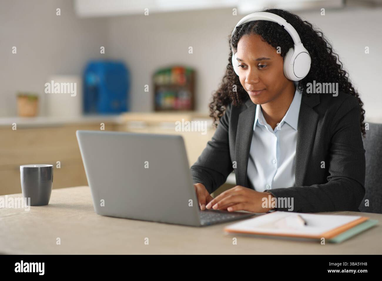 Tele executive nero che lavora con laptop e cuffie in cucina a casa Foto Stock