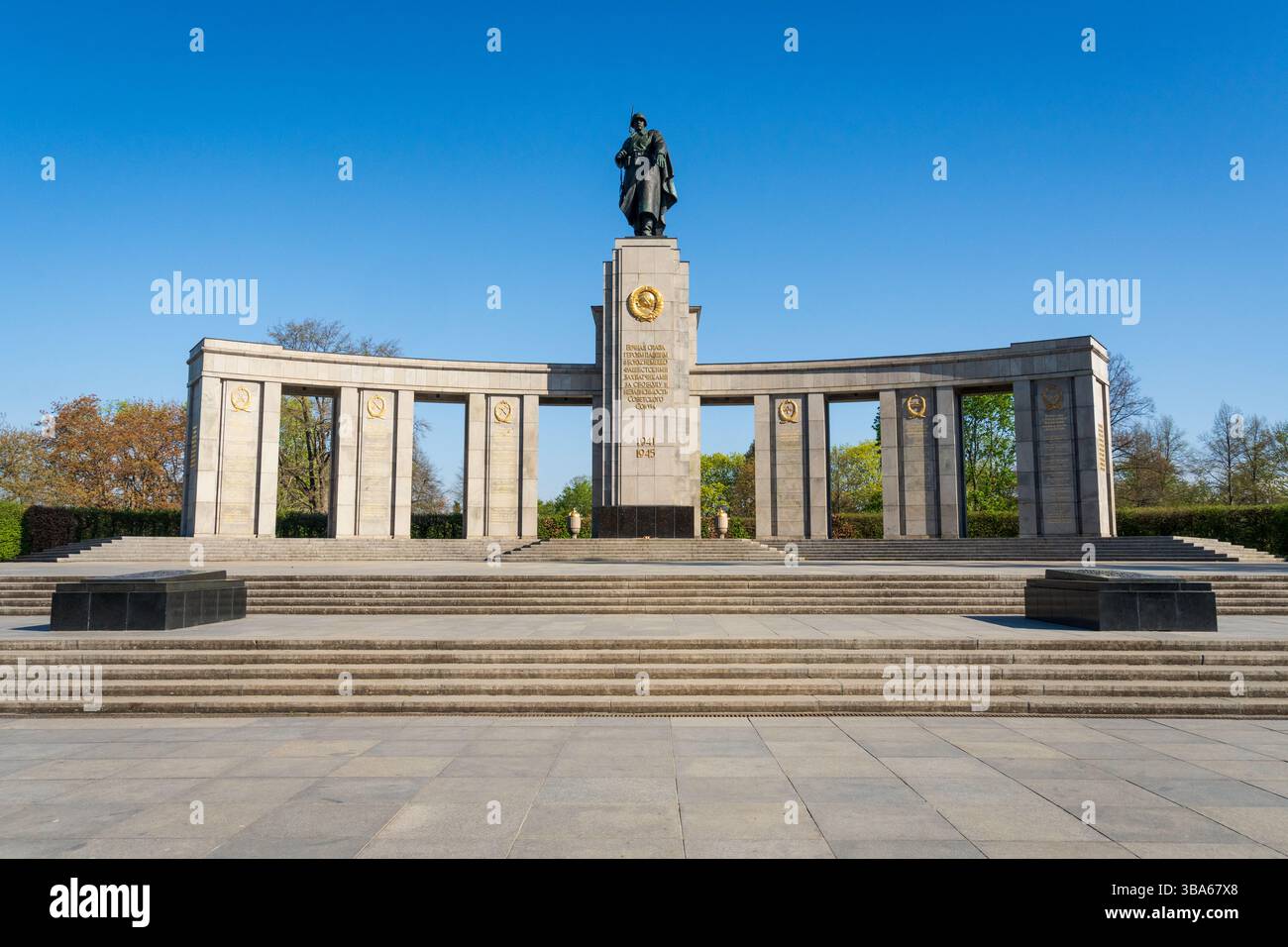 La colonnata semicircolare, la statua centrale e i gradini di pietra del Memoriale di Guerra Sovietico tra alberi verdi freschi, a Berlino, Germania. Foto Stock
