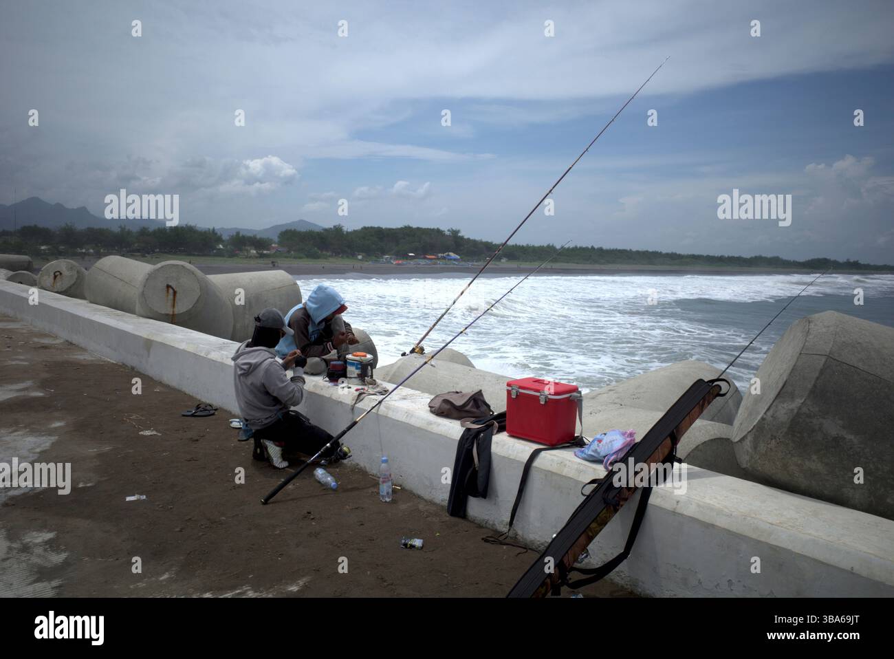 Yogyakarta - Indonesia, 20 aprile 2025: Pescatori che pescano a Congot Beach, Kulon Progo, Yogyakarta, Indonesia con struttura di demolitore a onde di cemento tetrapod Foto Stock
