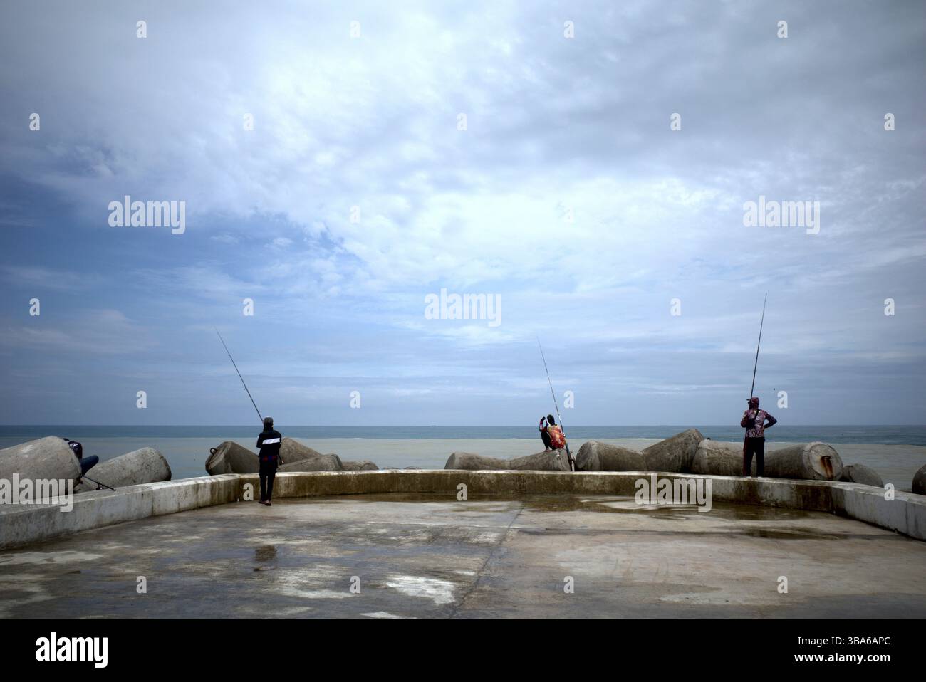 Yogyakarta - Indonesia, 20 aprile 2025: Pescatori che pescano a Congot Beach, Kulon Progo, Yogyakarta, Indonesia con struttura di demolitore a onde di cemento tetrapod Foto Stock
