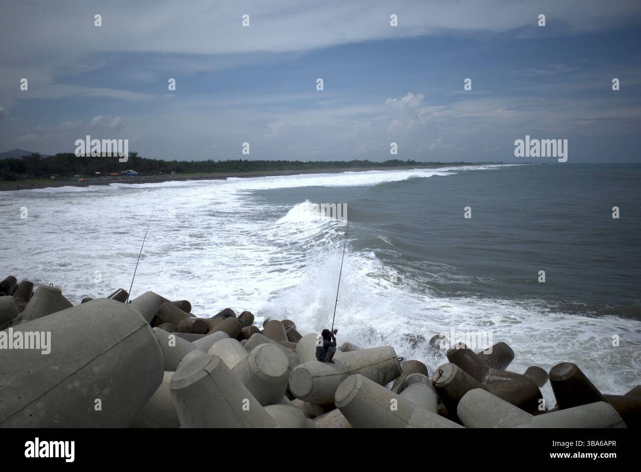 Pescatori che pescano a Congot Beach, Kulon Progo, Yogyakarta, Indonesia, con strutture per rompere le onde di cemento tetrapodico. Foto Stock