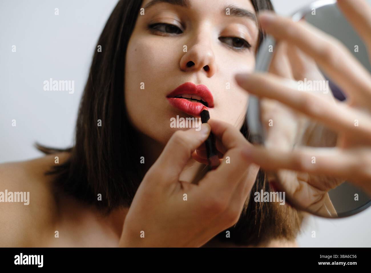 Applicare il rossetto in una stanza ben illuminata con uno specchio Foto Stock