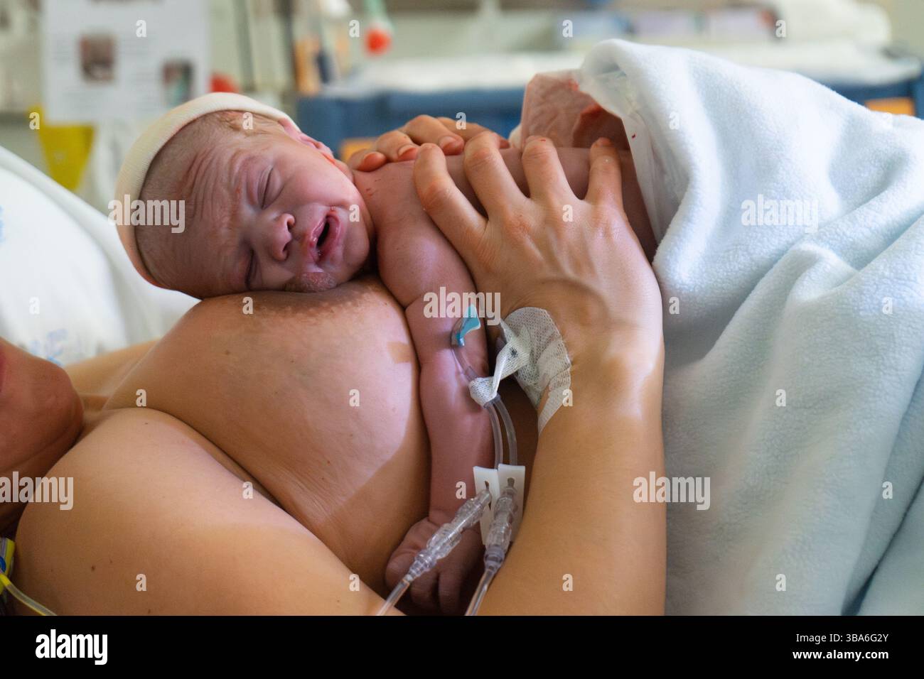 La madre abbraccia il bambino appena nato che riposa sul petto, pochi istanti dopo il parto in una stanza d'ospedale Foto Stock