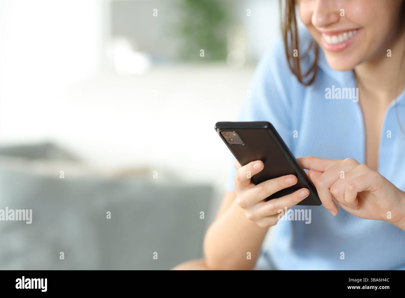 Primo piano di una donna felice che tiene e usa lo smartphone a casa Foto Stock