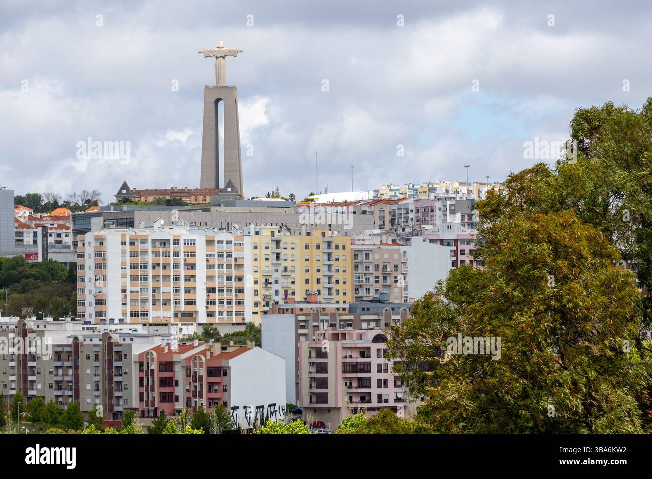 Statua di Cristo rei che si erge in alto sul paesaggio urbano di almada sotto il cielo nuvoloso, l'area metropolitana di lisbona, portogallo Foto Stock