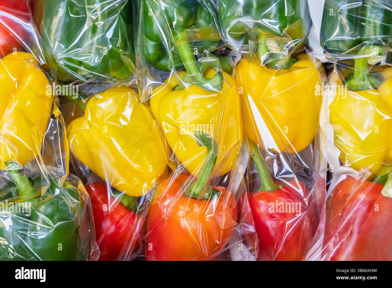 Peperoni gialli, verdi e rossi avvolti in plastica in un negozio di alimentari Foto Stock