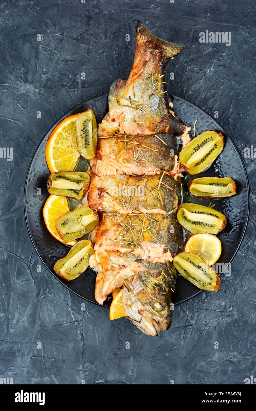 Piatto di trota intera al forno, servito con kiwi e arancia. Foto Stock