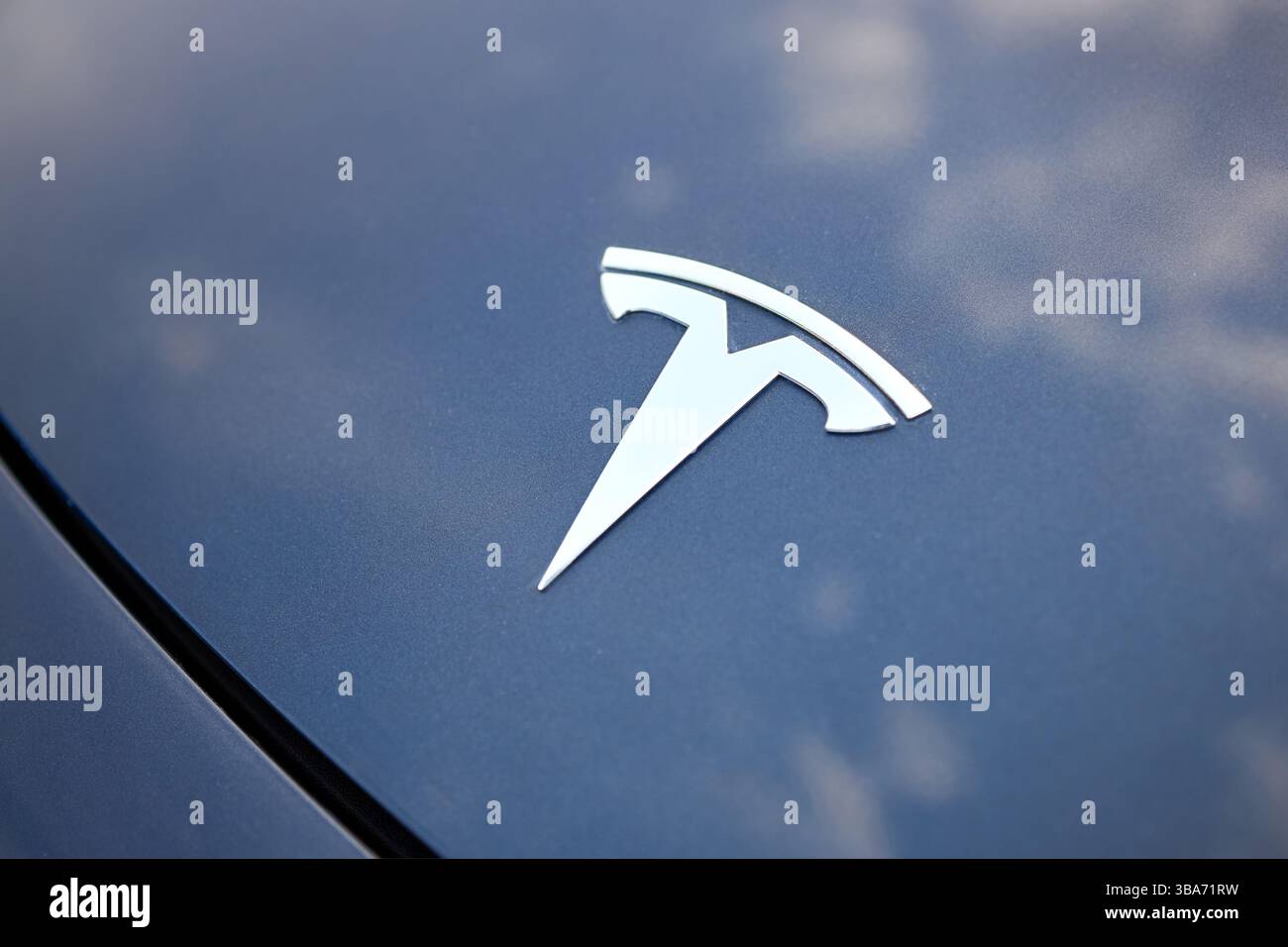 Berlino, Germania - 4 maggio 2024: Tesla Model 3 54 kWh Standard Range Plus 2019. Logo del marchio Tesla sul cofano dell'auto con cielo blu e riflessi delle nuvole Foto Stock