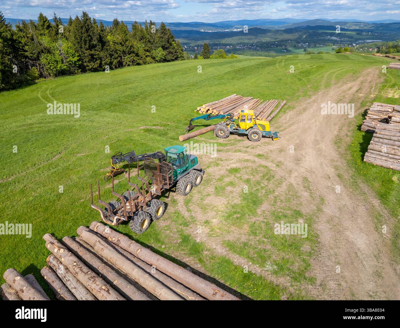 Vista aerea di un prato con trattori e gru circondato da alberi abbattuti vicino a un'area forestale, che mostra lavori forestali e macchinari sotto un summ trasparente Foto Stock