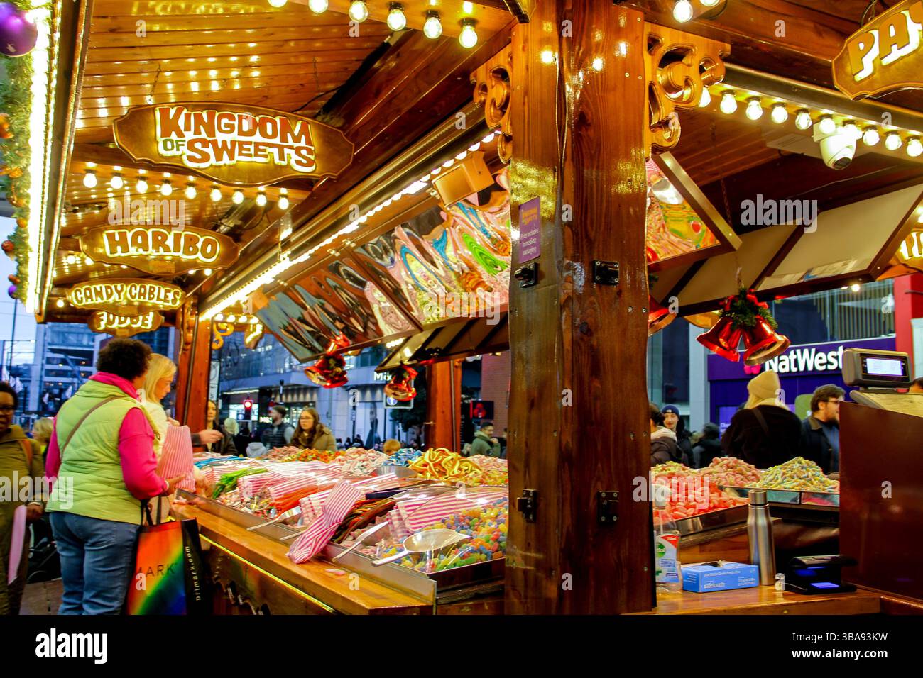 Piccadilly Garden: Luci luminose e un negozio di dolci al mercatino di Natale di Manchester, divertimento per famiglie con fascino stagionale. Foto Stock
