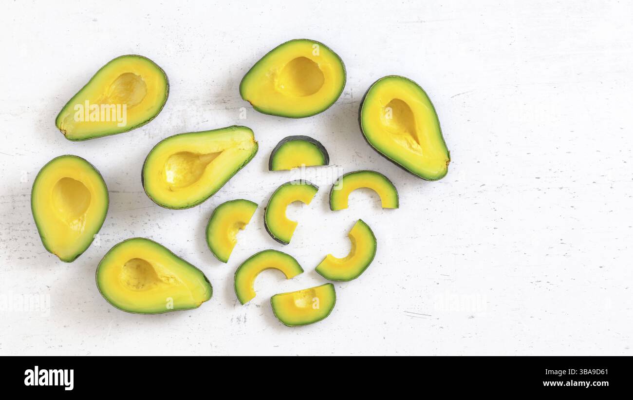 Vista dall'alto verso il basso, metà avocado e fette, su una tavola da lavoro bianca, la polpa di frutta ha un colore verde e giallo vibrante, spazio per il testo a destra, Liptovsky Hradok Foto Stock