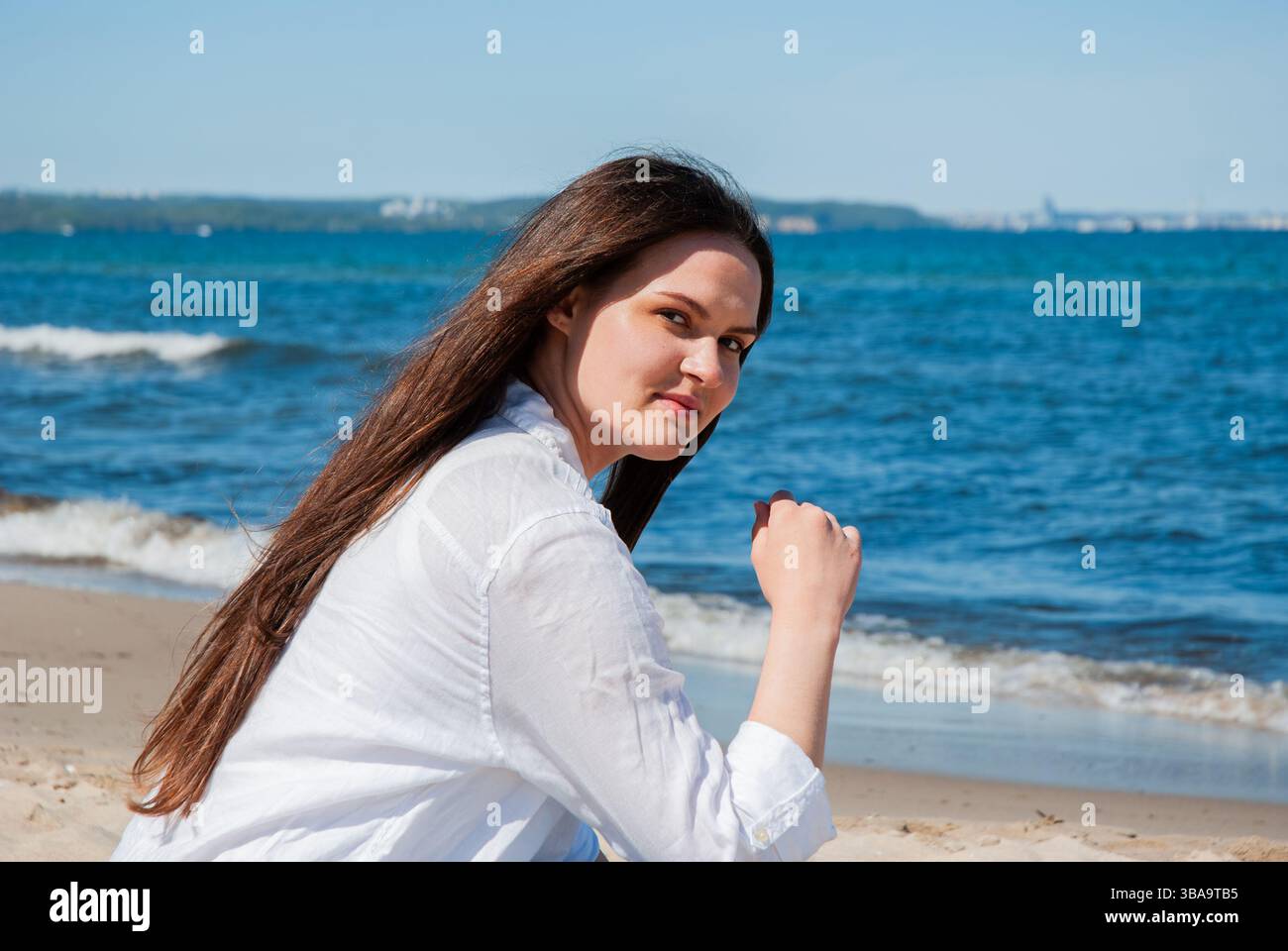 Giovane donna caucasica che si gode una giornata di sole sulla spiaggia con cieli azzurri e onde oceaniche che creano uno sfondo sereno e rilassante. Nomade digitale Foto Stock