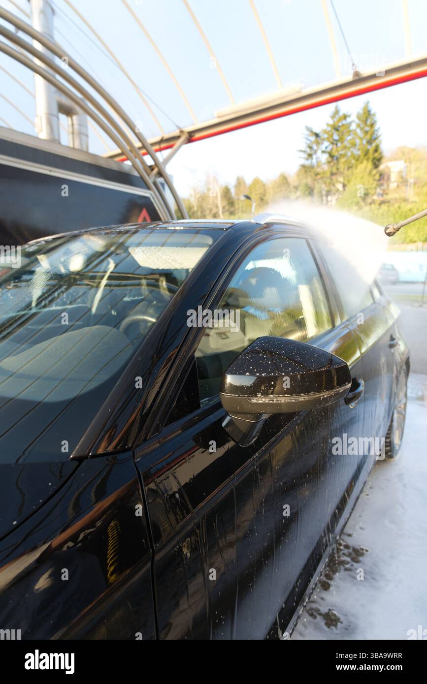 Una persona sta lavando un'auto nera con un tubo dell'acqua ad alta pressione Foto Stock