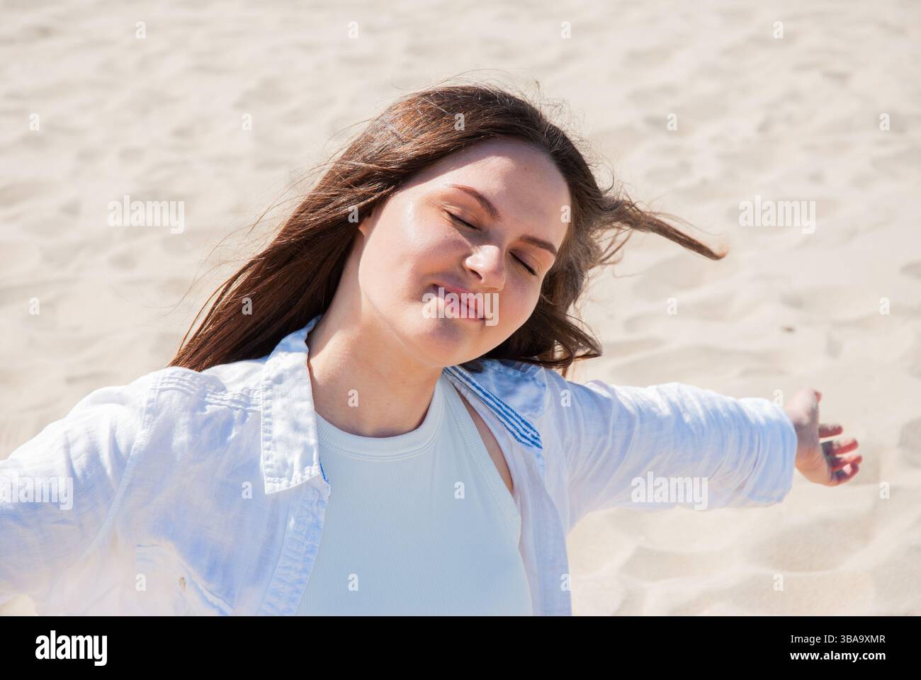 Giovane donna caucasica che si gode il sole sulla spiaggia di sabbia con le braccia aperte e gli occhi chiusi, abbracciando relax e libertà. Stile di vita digitale nomade. Telecomando WO Foto Stock
