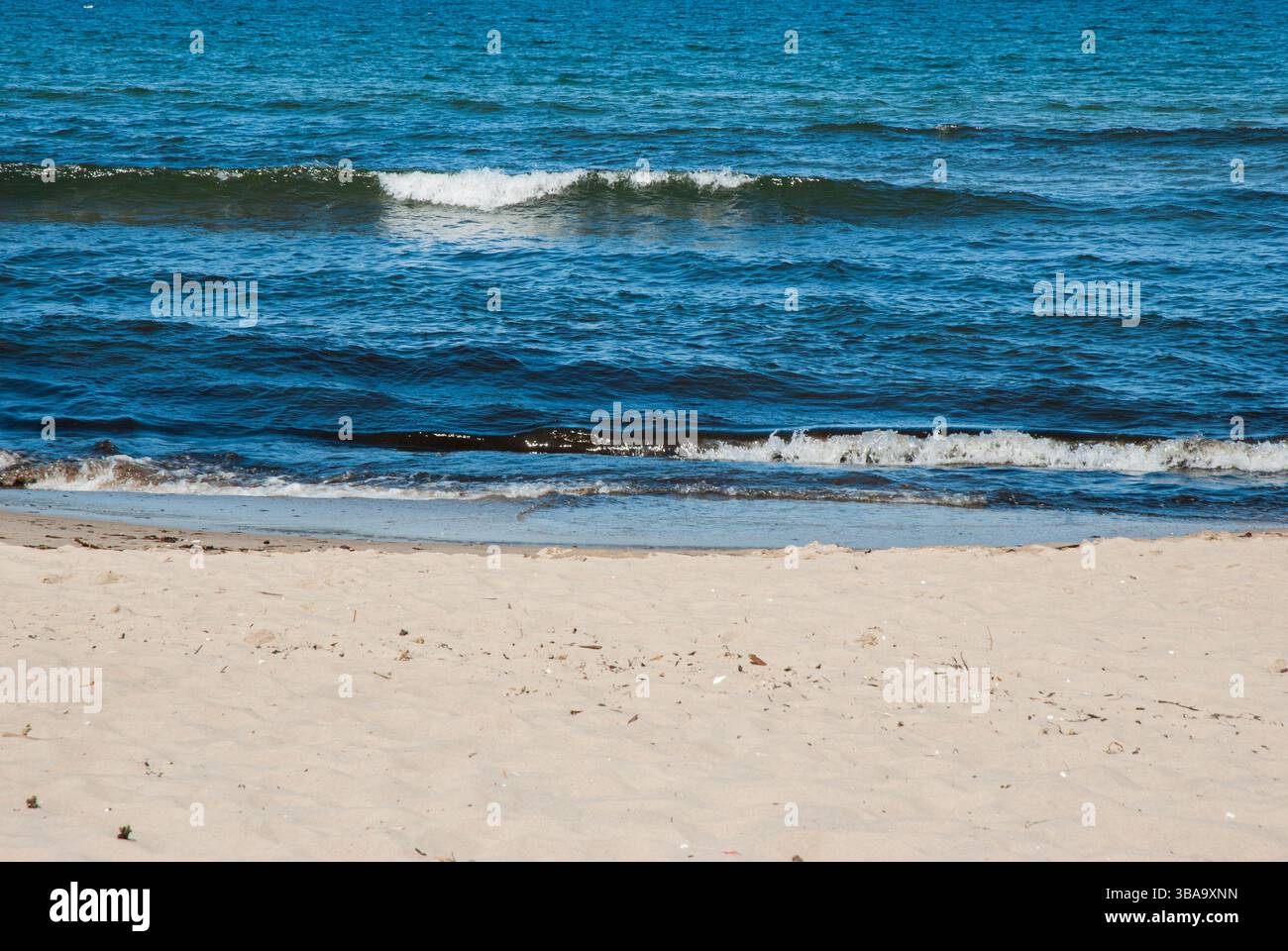 Tranquilla costa sabbiosa con dolci onde oceaniche in una tranquilla giornata di sole che sfoggia acque blu incontaminate e sabbia dorata di una spiaggia isolata. Foto Stock