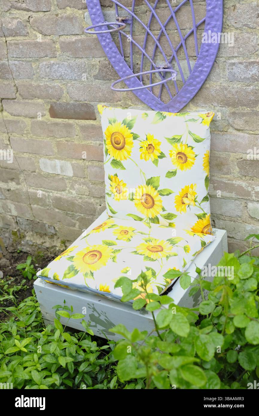 Bizzarro sedile da giardino realizzato con una piantatrice riutilizzata e due cuscini in vinile con stampa girasole fatti a mano, adagiati su una rustica parete in mattoni Foto Stock