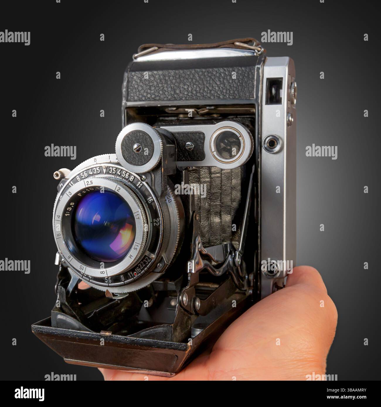 Una mano tiene in mano una fotocamera vintage, che mette in mostra il suo complesso obiettivo e il design del corpo in un ambiente ben illuminato che ne migliora le caratteristiche. Foto Stock