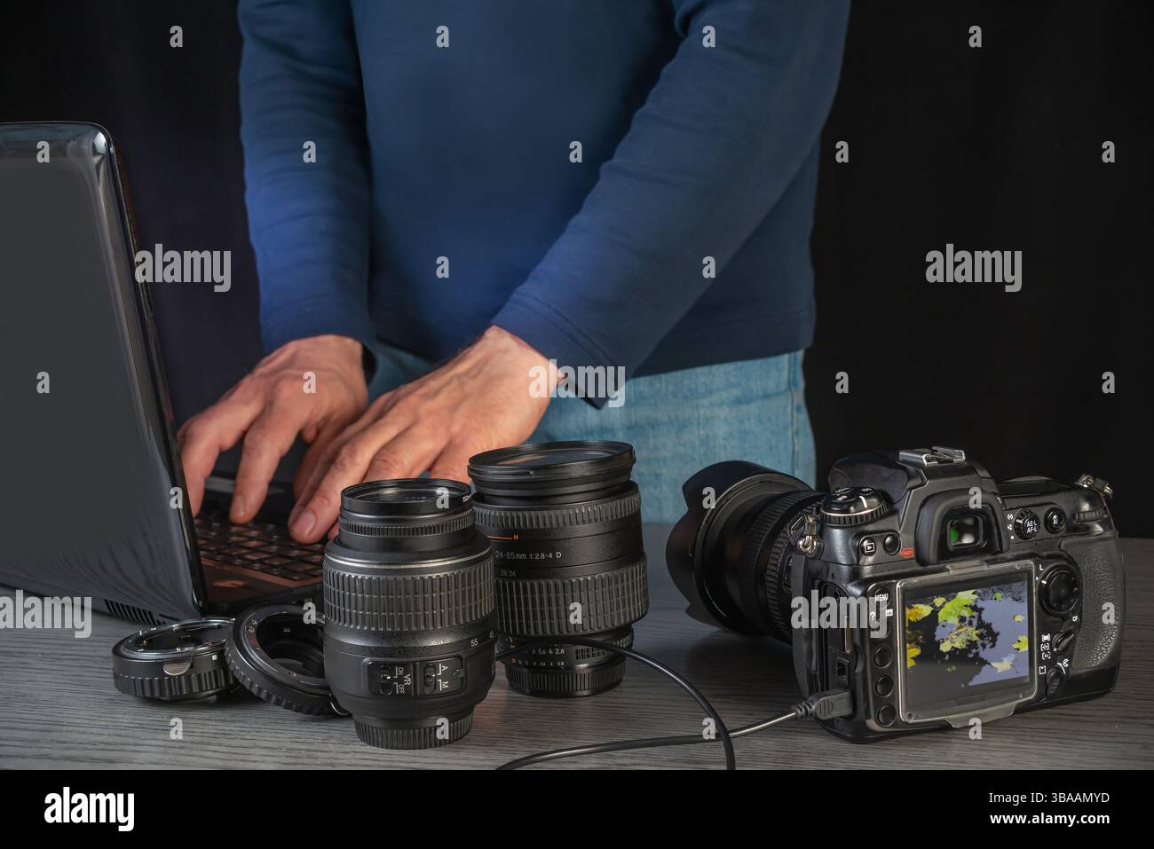 Editing professionale creativo di immagini utilizzando un computer portatile circondato da obiettivi della fotocamera e una reflex digitale, in preparazione per un nuovo progetto fotografico. Foto Stock