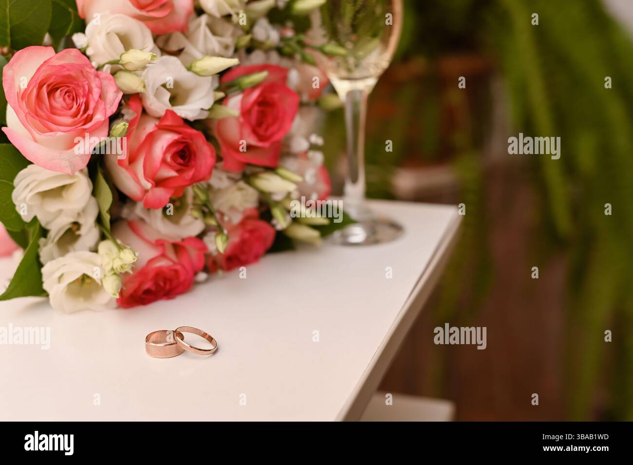 Le fedi nuziali, il bouquet di rose e il bicchiere di champagne sul tavolo creano una composizione elegante. La scena cattura l'amore, la celebrazione e i dettagli romantici con raffinatezza Foto Stock