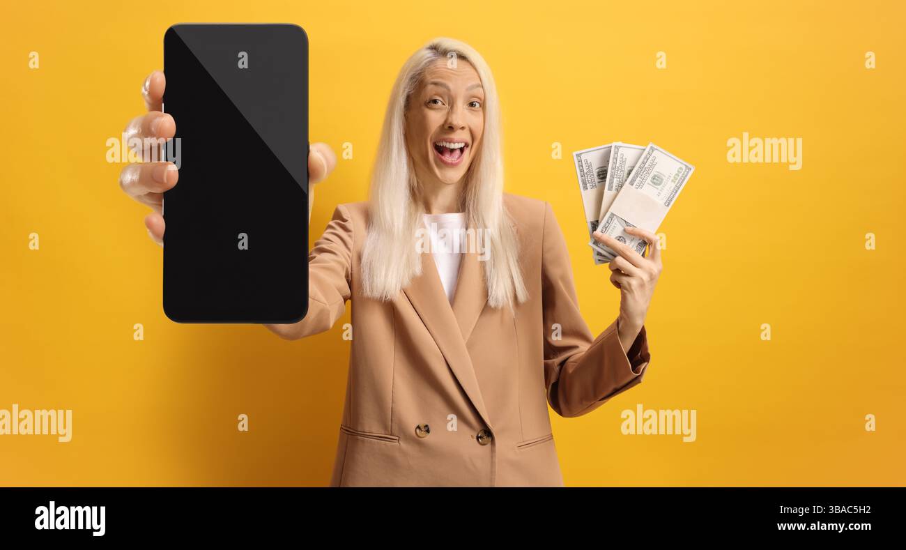 Giovane donna felice con soldi e smartphone su sfondo giallo Foto Stock