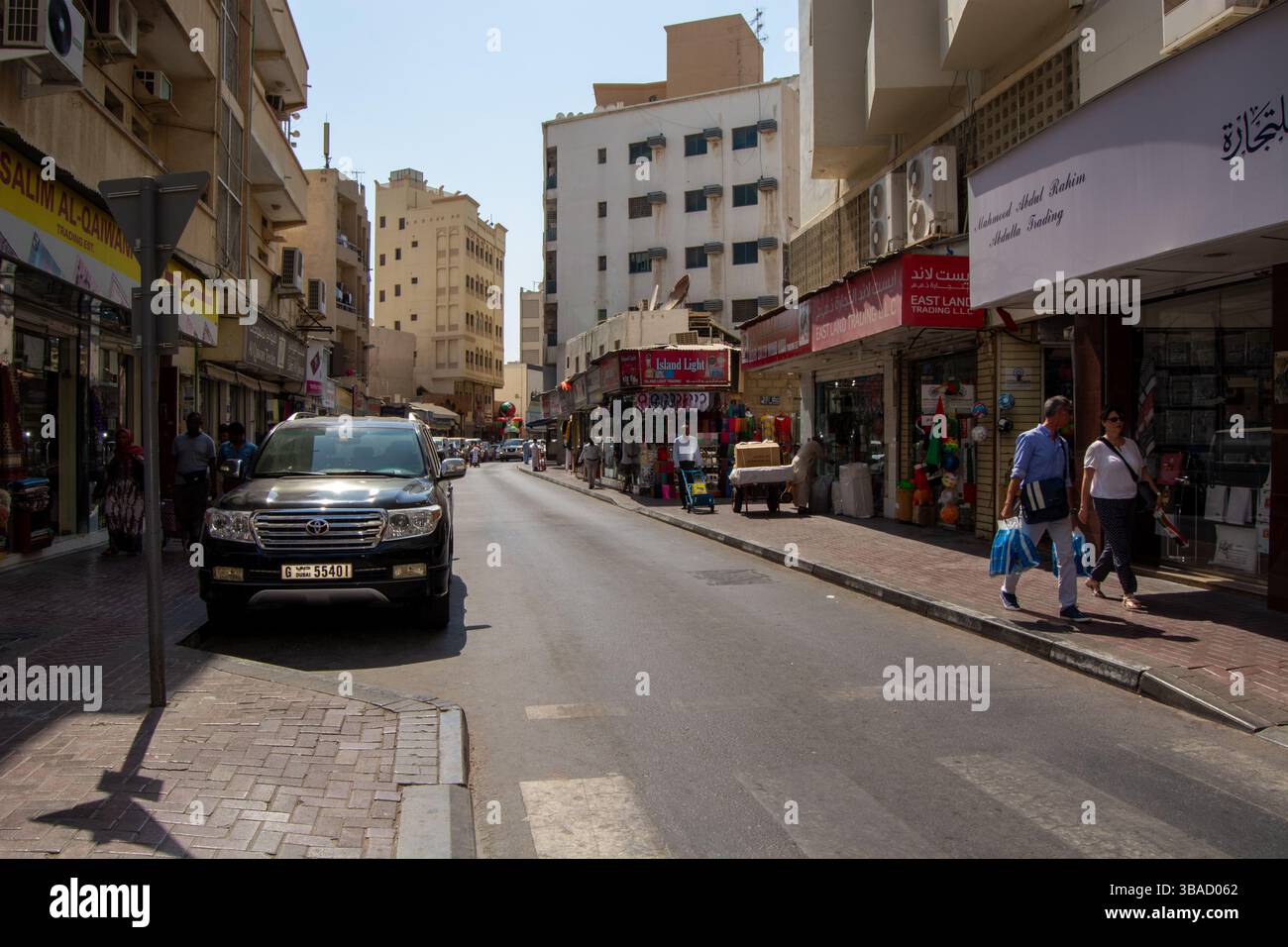 Una vivace scena di strada in una città con negozi su entrambi i lati, con un SUV parcheggiato e pedoni a piedi. Gli edifici sono un mix di moderno e tradizionale Foto Stock