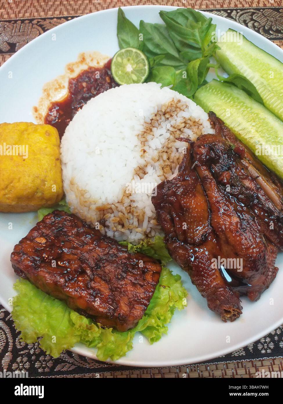Cibo indonesiano - riso al vapore con Ayam Bakar, Tempe Bacem e Tahu Goreng insieme a verdure crude e sambal di peperoncino rosso Foto Stock
