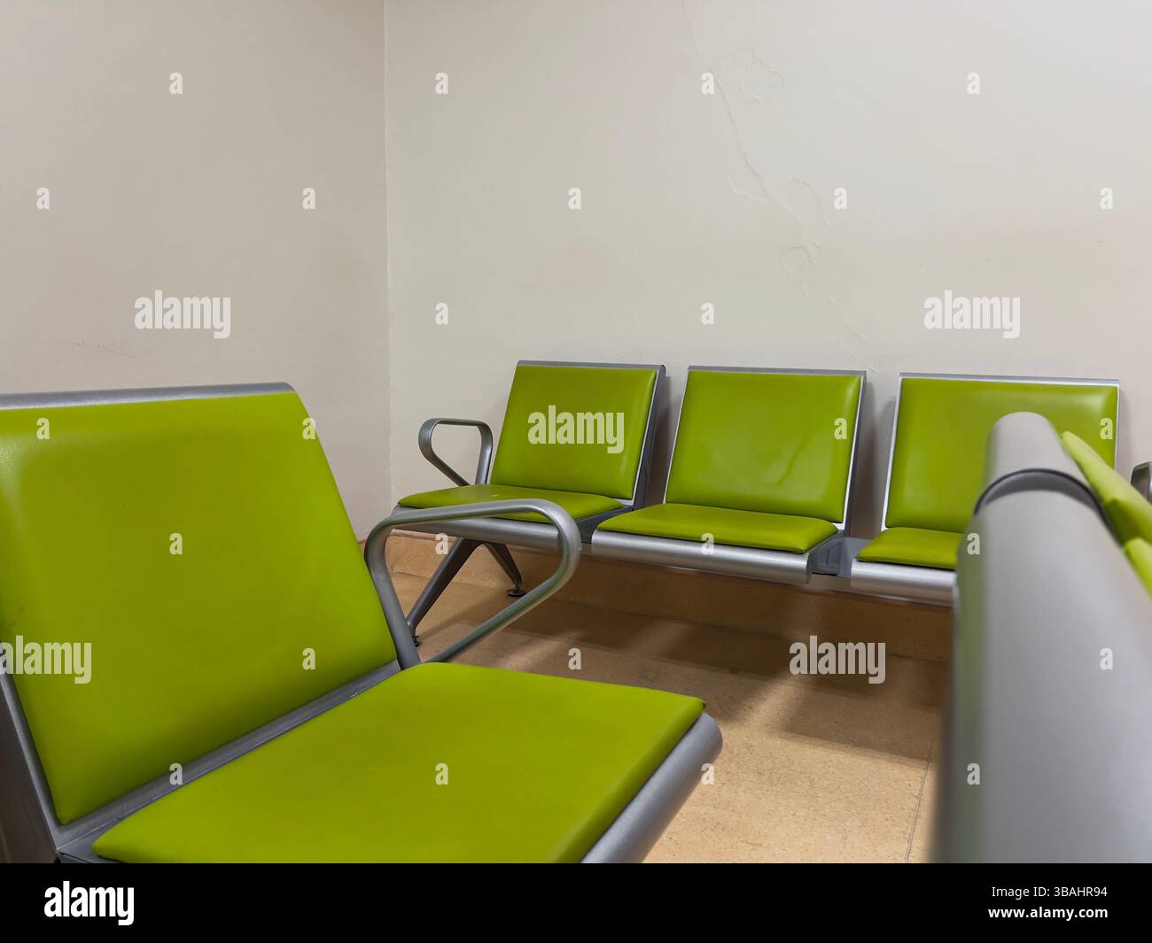 Una sala d'attesa pulita e moderna con sedie verdi luminose con telai metallici, disposte contro una parete neutra. Foto Stock