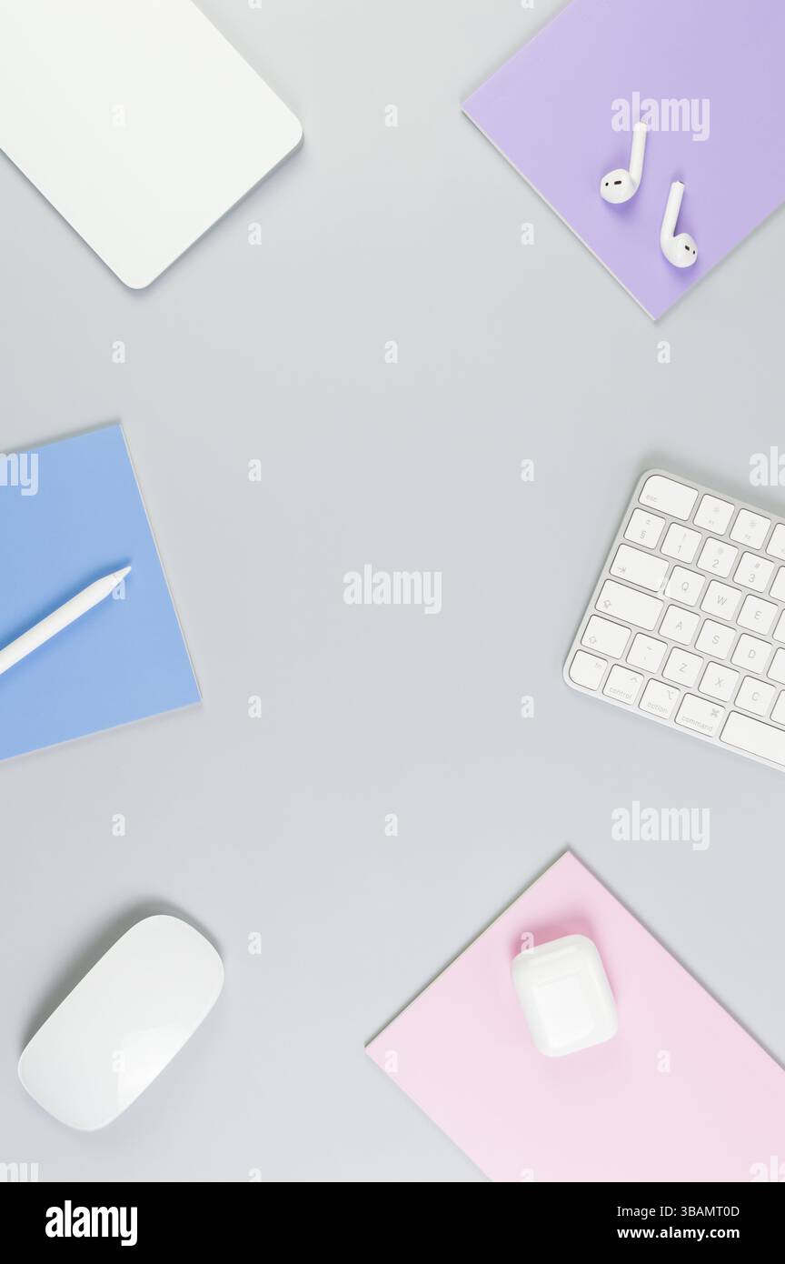 Vista dall'alto di tastiera bianca, mouse, touchpad, custodia per auricolari, penna su sfondo grigio. Quaderni viola, rosa e blu, ufficio moderno, scuola. Foto Stock