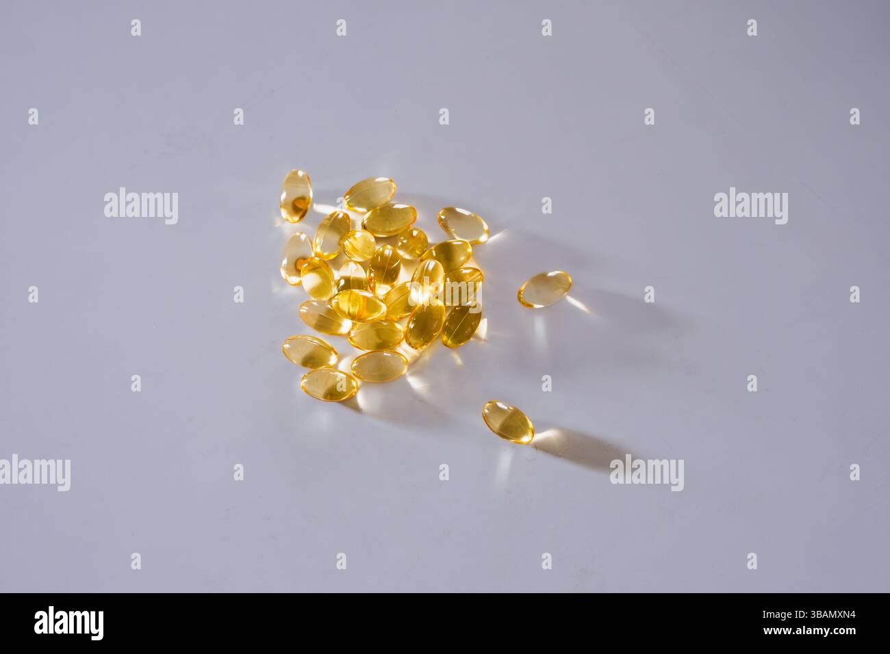 Una raccolta di capsule softgel gialle-dorate traslucide sparse su una superficie bianca pulita. Foto Stock