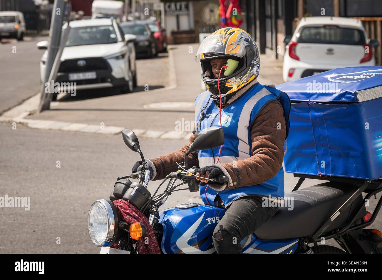 Un motociclista che ha un telefono bloccato nel casco. Il quartiere dell'Osservatorio, noto per la sua scena bohémien e artistica. Città del Capo Foto Stock