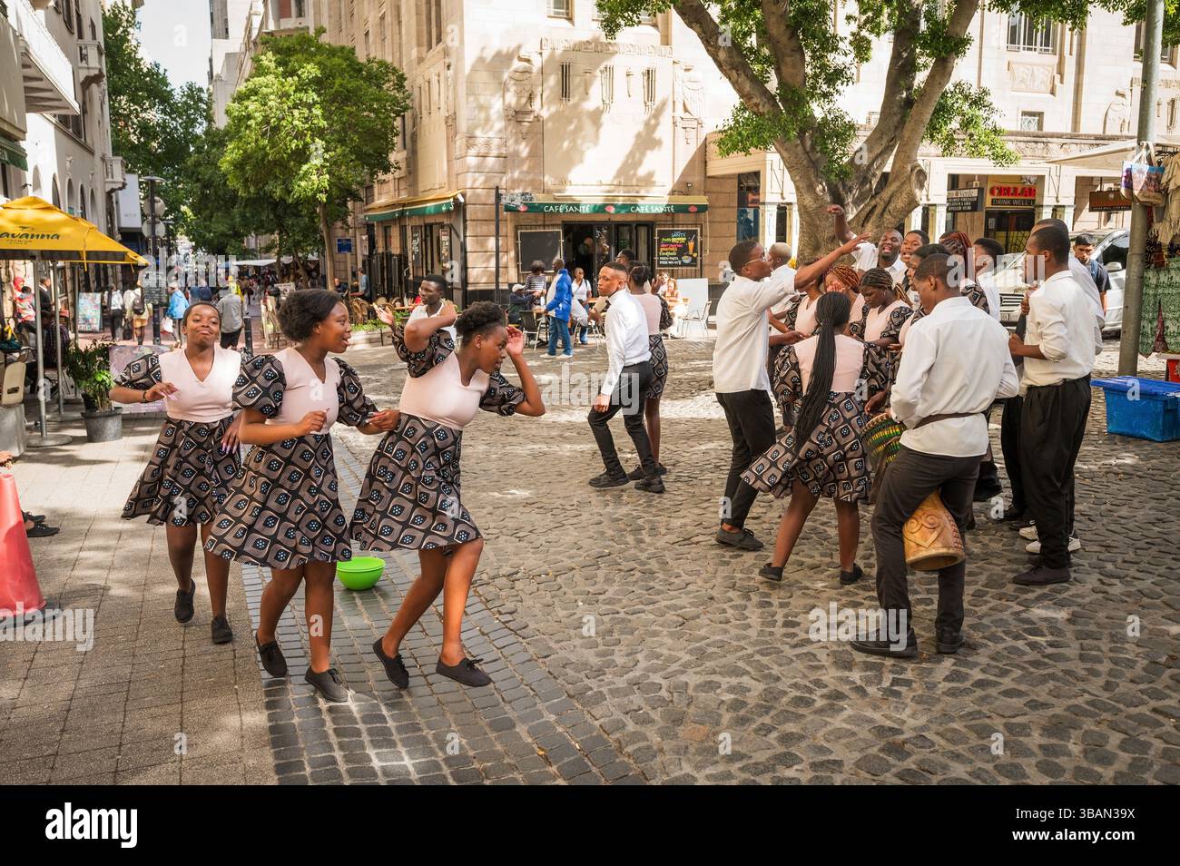Un tradizionale coro africano per bambini si esibisce tra i venditori ambulanti e i negozi di artigianato a Greenmarket Square, nel centro di città del Capo, in Sudafrica. Foto Stock