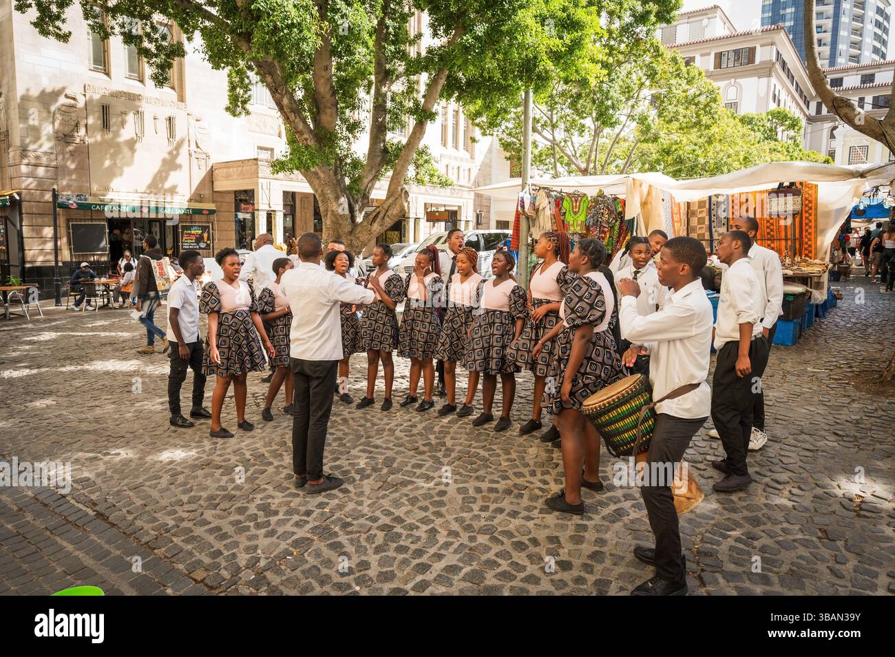 Un tradizionale coro africano per bambini si esibisce tra i venditori ambulanti e i negozi di artigianato a Greenmarket Square, nel centro di città del Capo, in Sudafrica. Foto Stock