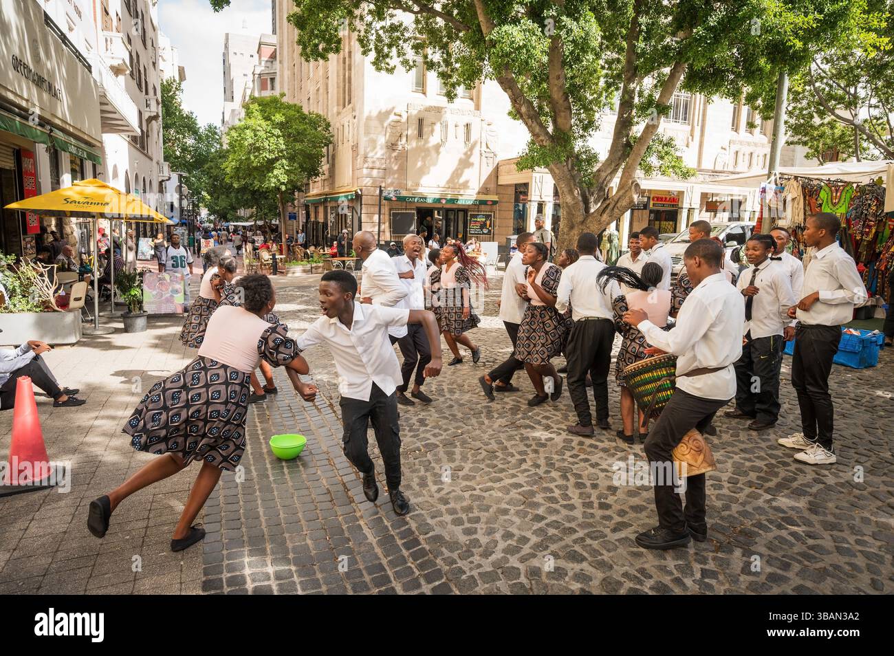 Un tradizionale coro africano per bambini si esibisce tra i venditori ambulanti e i negozi di artigianato a Greenmarket Square, nel centro di città del Capo, in Sudafrica. Foto Stock