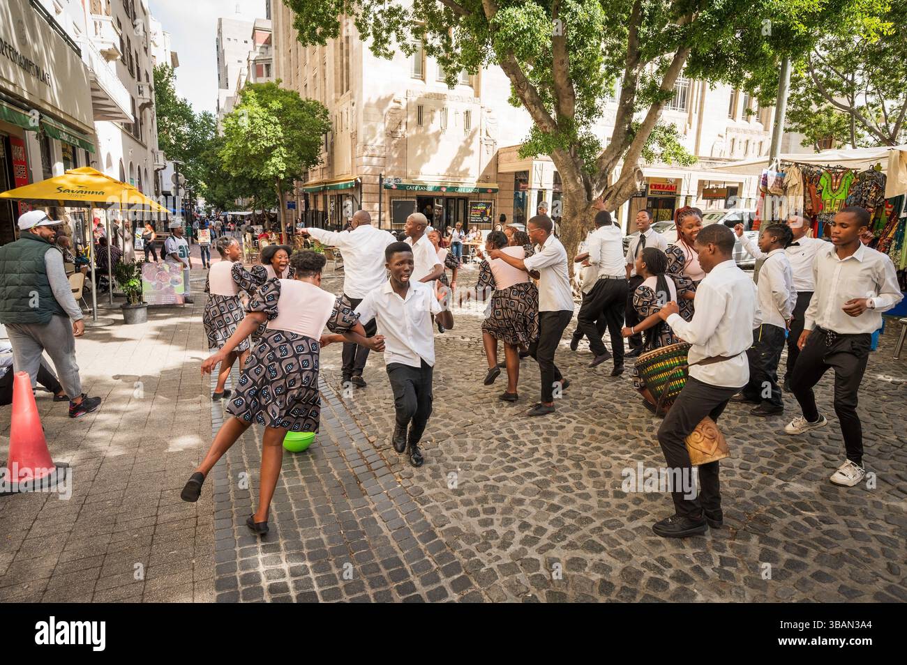 Un tradizionale coro africano per bambini si esibisce tra i venditori ambulanti e i negozi di artigianato a Greenmarket Square, nel centro di città del Capo, in Sudafrica. Foto Stock