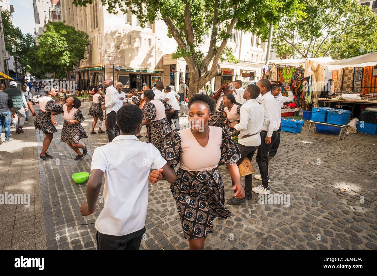 Un tradizionale coro africano per bambini si esibisce tra i venditori ambulanti e i negozi di artigianato a Greenmarket Square, nel centro di città del Capo, in Sudafrica. Foto Stock