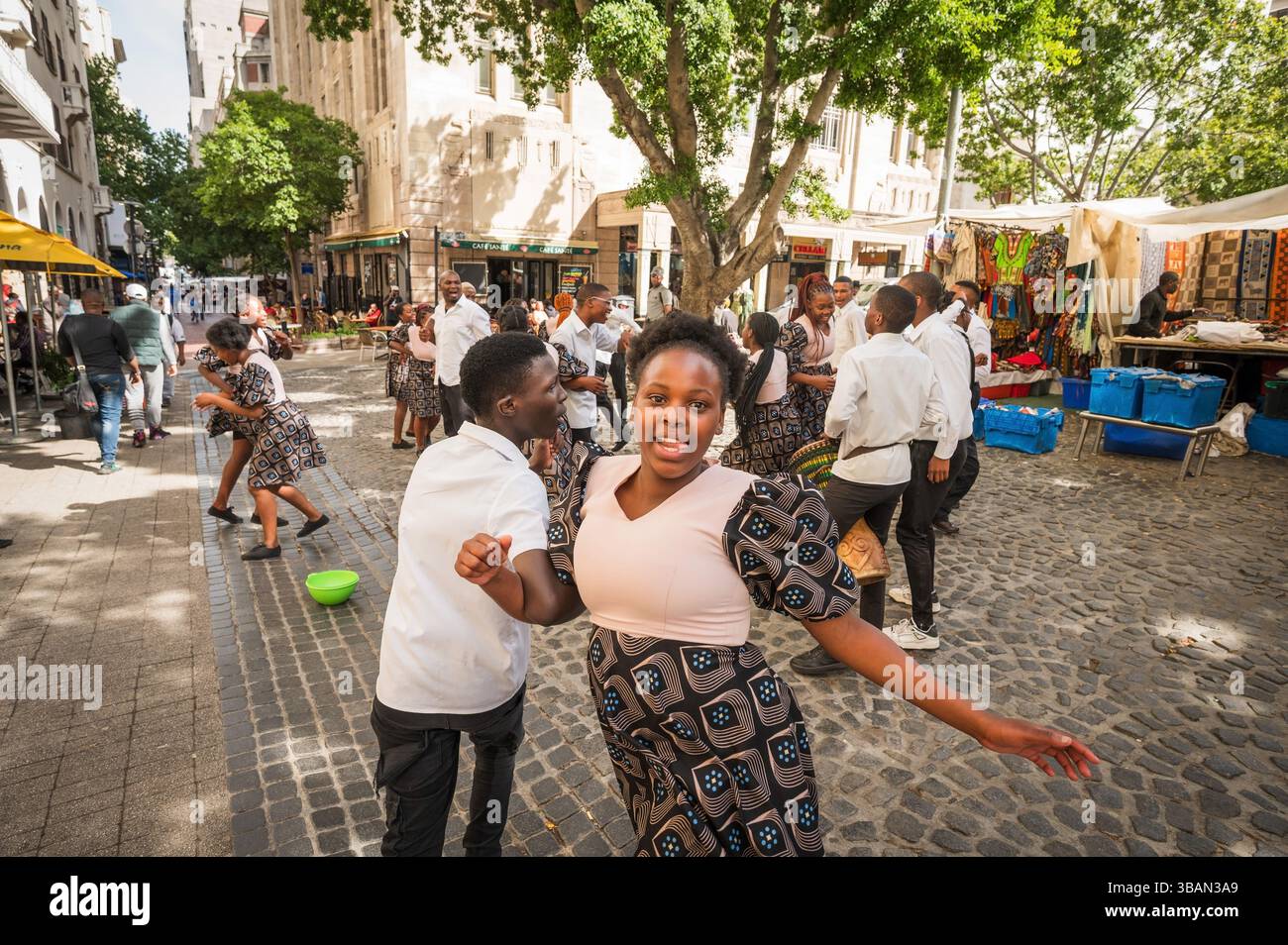 Un tradizionale coro africano per bambini si esibisce tra i venditori ambulanti e i negozi di artigianato a Greenmarket Square, nel centro di città del Capo, in Sudafrica. Foto Stock