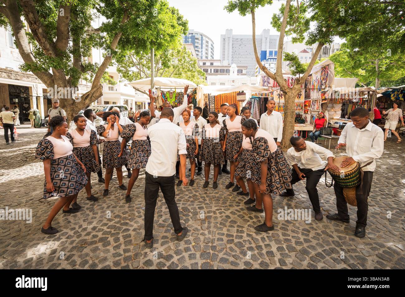 Un tradizionale coro africano per bambini si esibisce tra i venditori ambulanti e i negozi di artigianato a Greenmarket Square, nel centro di città del Capo, in Sudafrica. Foto Stock