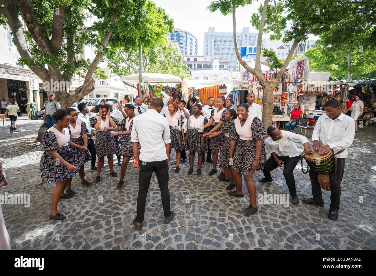 Un tradizionale coro africano per bambini si esibisce tra i venditori ambulanti e i negozi di artigianato a Greenmarket Square, nel centro di città del Capo, in Sudafrica. Foto Stock