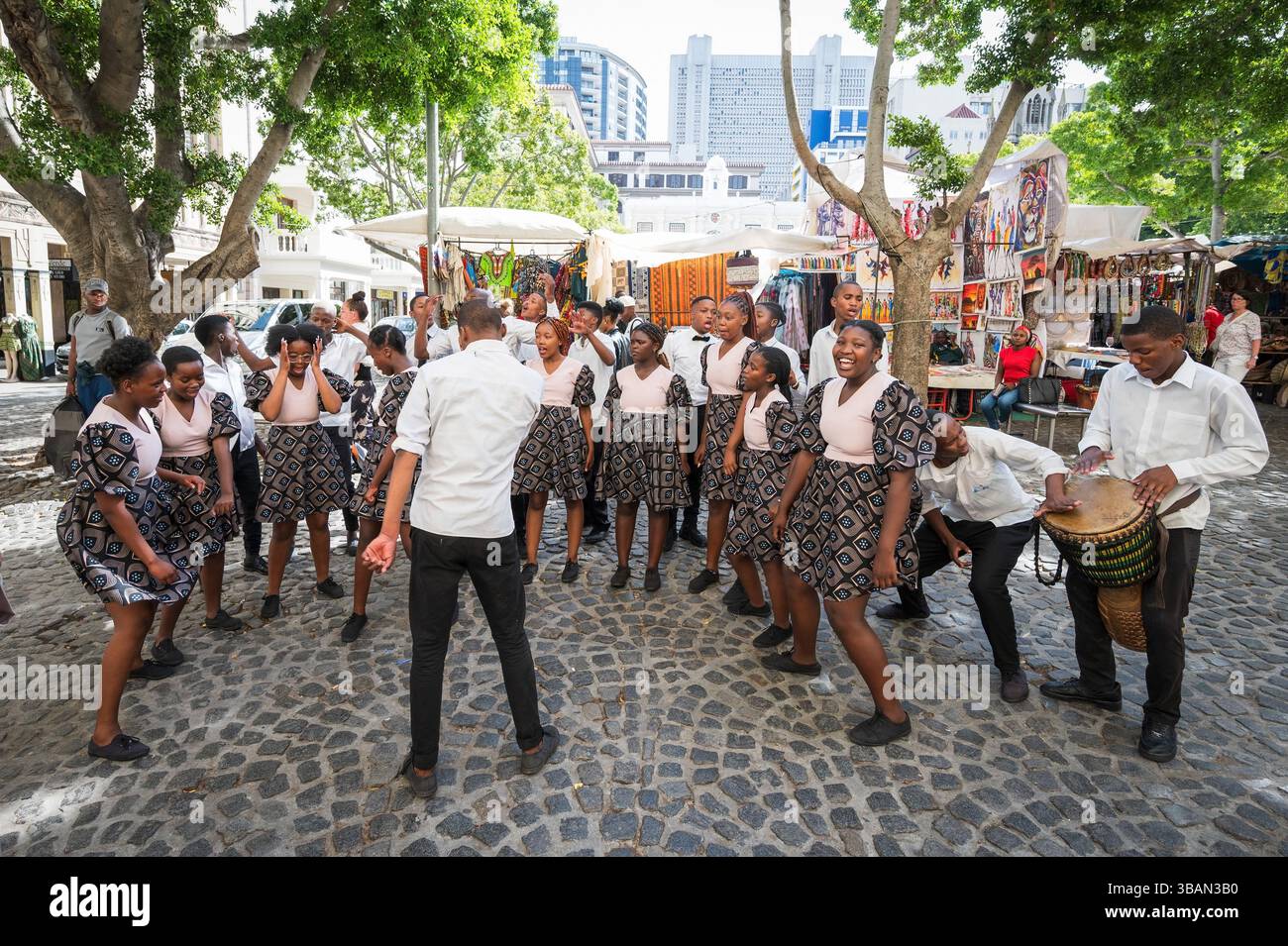 Un tradizionale coro africano per bambini si esibisce tra i venditori ambulanti e i negozi di artigianato a Greenmarket Square, nel centro di città del Capo, in Sudafrica. Foto Stock