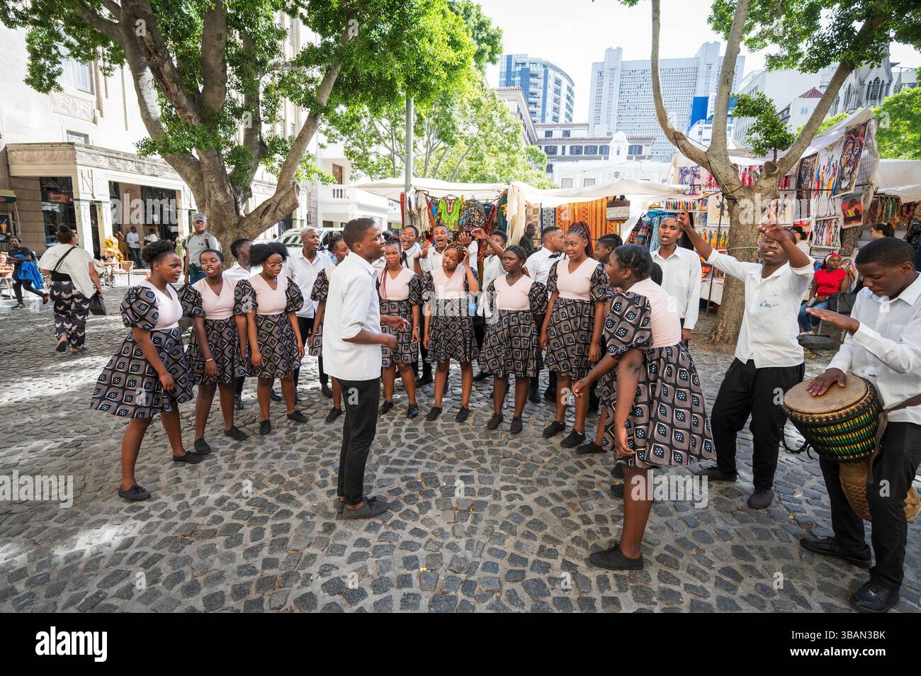 Un tradizionale coro africano per bambini si esibisce tra i venditori ambulanti e i negozi di artigianato a Greenmarket Square, nel centro di città del Capo, in Sudafrica. Foto Stock