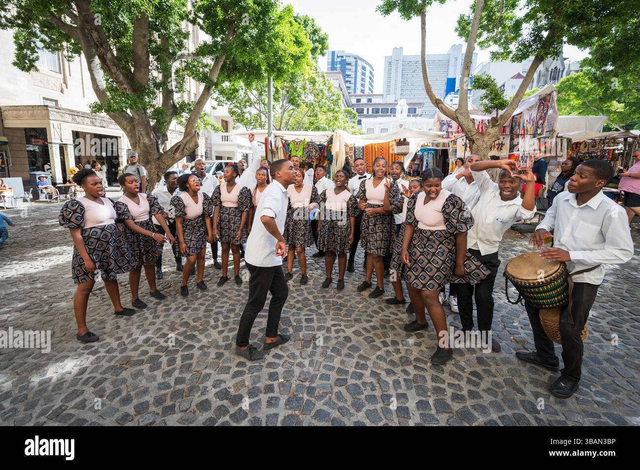 Un tradizionale coro africano per bambini si esibisce tra i venditori ambulanti e i negozi di artigianato a Greenmarket Square, nel centro di città del Capo, in Sudafrica. Foto Stock