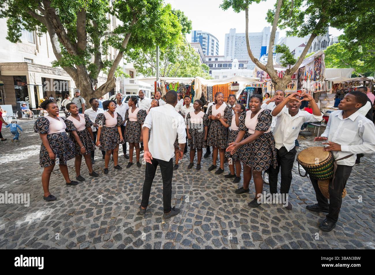 Un tradizionale coro africano per bambini si esibisce tra i venditori ambulanti e i negozi di artigianato a Greenmarket Square, nel centro di città del Capo, in Sudafrica. Foto Stock