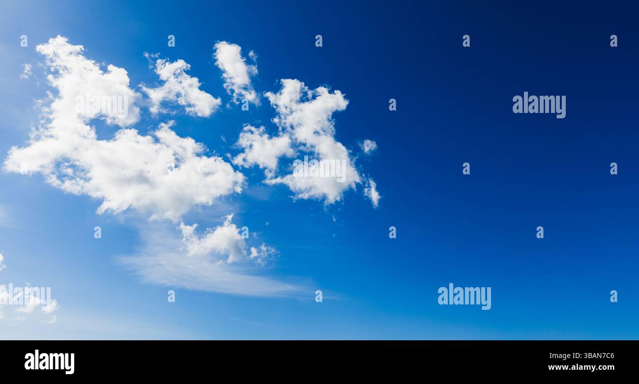 Un cielo blu sereno adornato da nuvole bianche e soffici che fluttuano tranquillamente, evocando un senso di pace e libertà durante una giornata di sole. bac panoramico Foto Stock