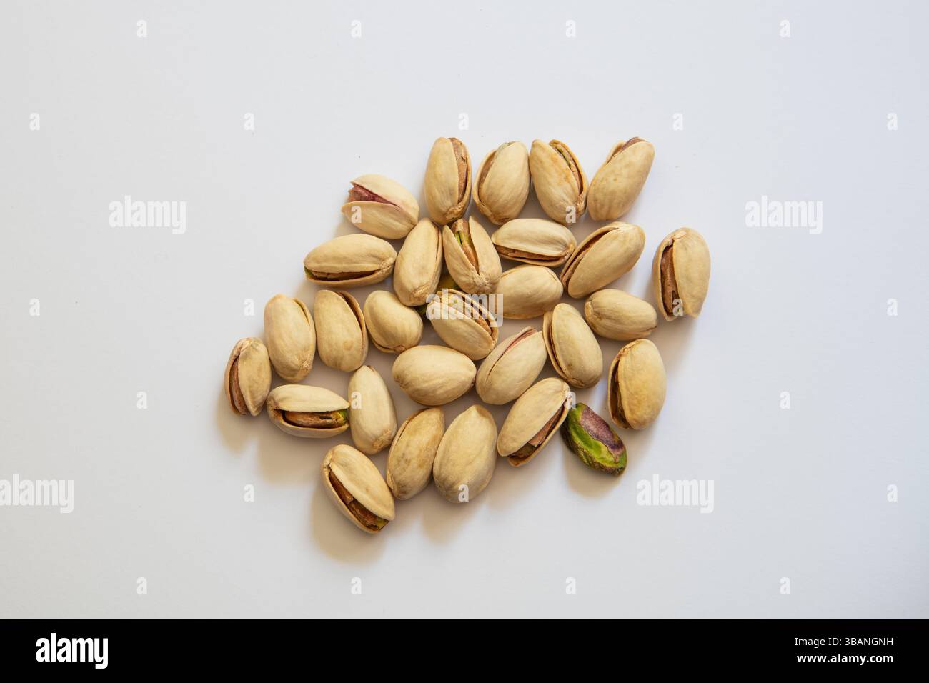 Nocciole di pistacchio naturali nelle conchiglie su sfondo bianco pulito. Uno spuntino sano a base vegetale presentato in uno stile semplice e minimalista. Foto Stock