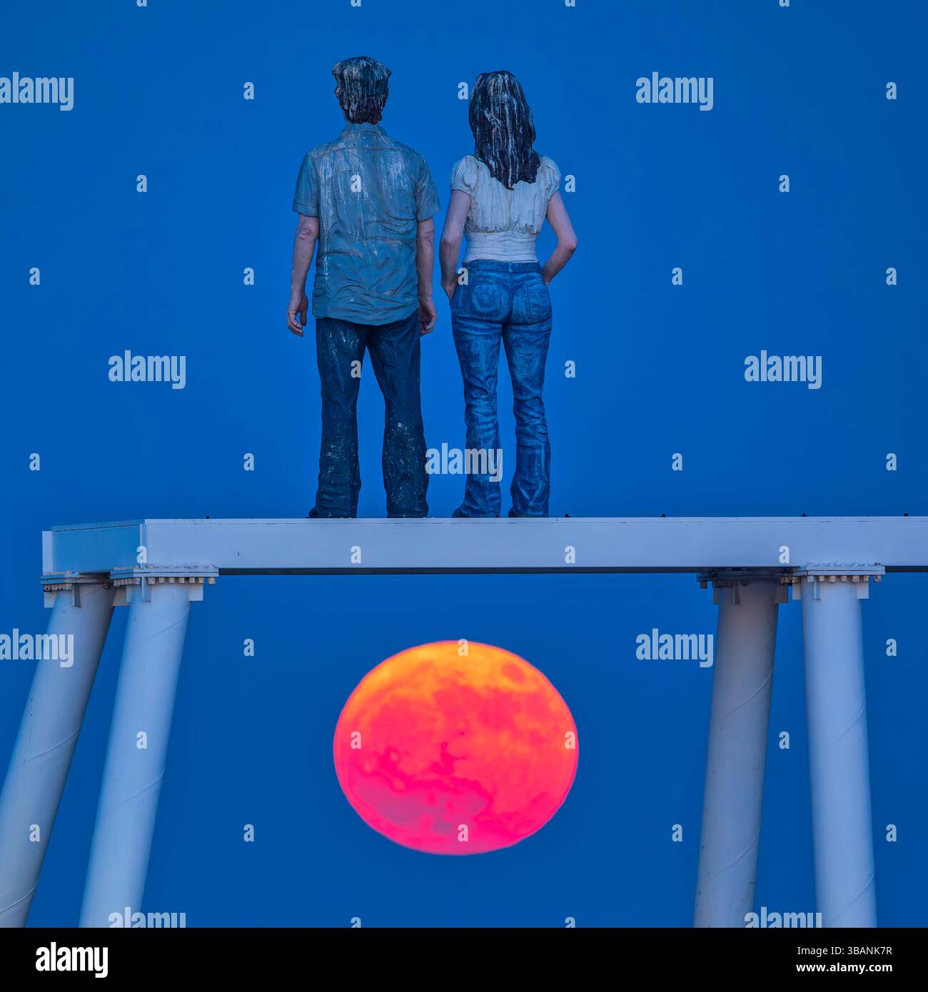Vista della luna piena "Flower Moon" che si innalza al crepuscolo sopra la scultura di "coppia" a Newbiggin-by-the-Sea nel Northumberland in un cielo limpido Foto Stock